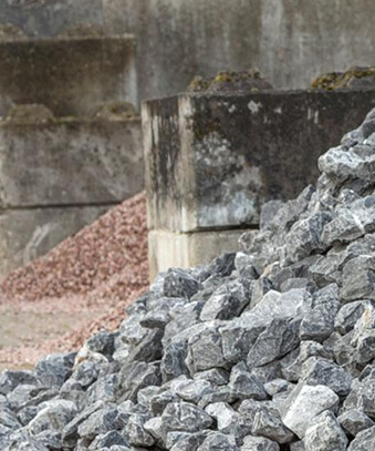 Pile of grey crushed stone aggregate at construction site with concrete wall and red gravel in background