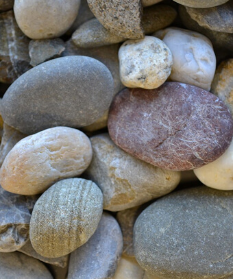 Close-up of smooth natural river stones and pebbles in various earth tones including grey, beige, and brown